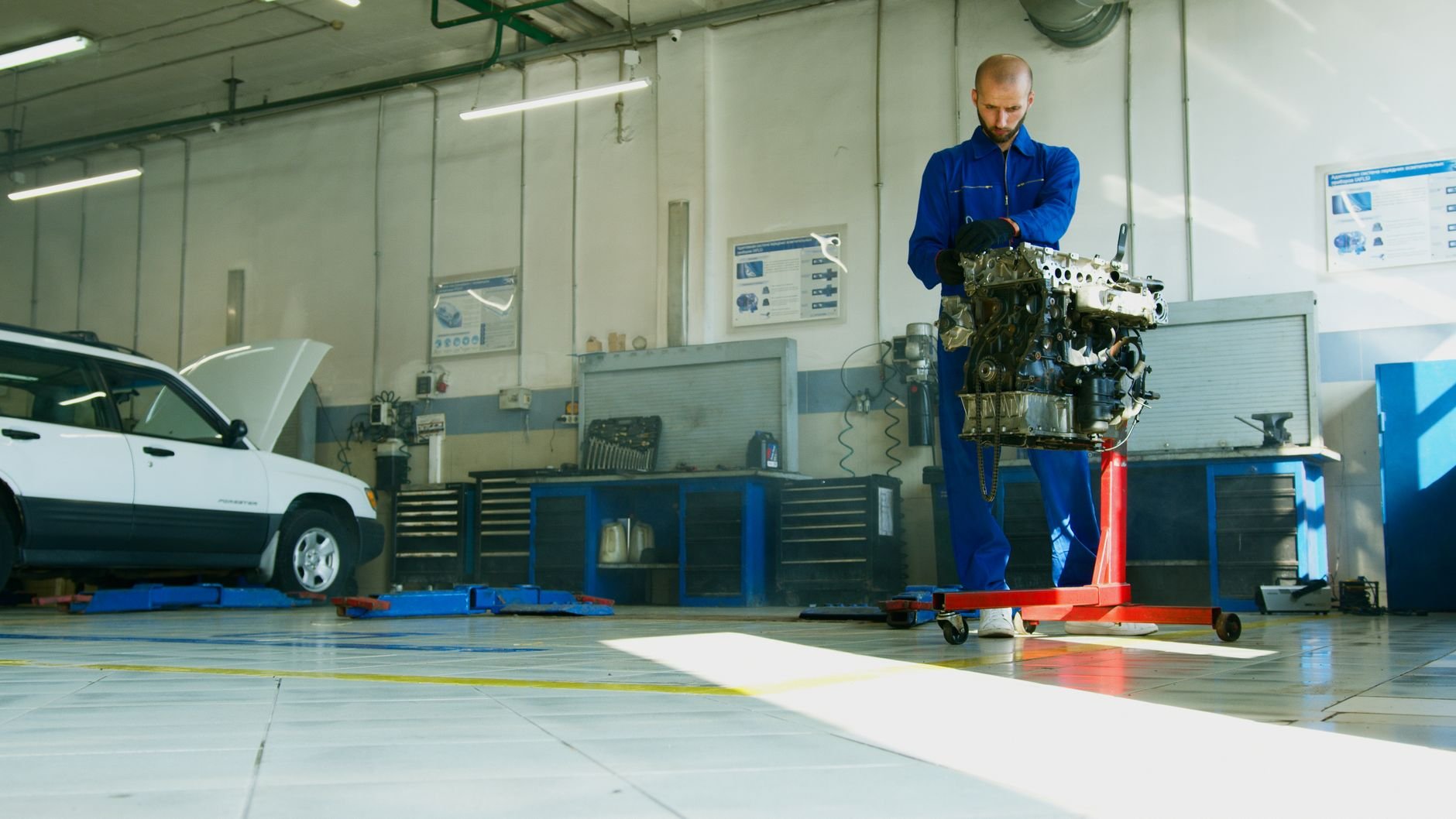 Mechanic lifting a car engine in a well-lit auto repair shop
